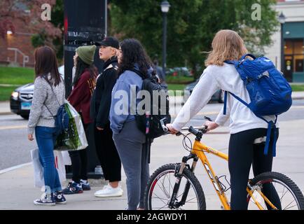 Storrs, CT USA. Okt 2019. Caucasain Studentin auf dem Fahrrad auf dem Campus Schnittpunkt mit vielfältigen Gruppe von Hispanischen und asiatischen Studenten warten. Stockfoto