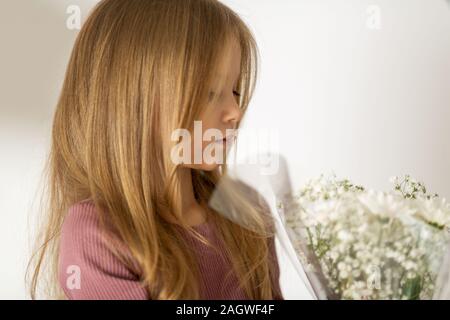 Schöne kleine blonde Mädchen mit langen Haaren, die einen weißen Hintergrund mit einem Blumenstrauß. Das Konzept der Kindheit Stockfoto