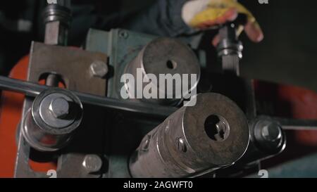 Schmiedewerkstatt auf dem Tisch. Arbeitnehmer Biegungen die Metallstange auf das schmiedeeiserne runde Biegemaschine. Herstellung von einem Designer Teil aus einer Metallstange. Stockfoto