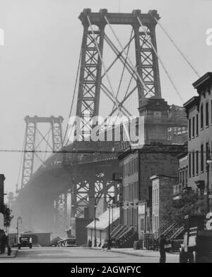 Die Williamsburg Bridge erhebt sich der Dunst über 8. Straße, die in Richtung Fluss hängen und hat Häuser und Geschäfte entlang. Stockfoto