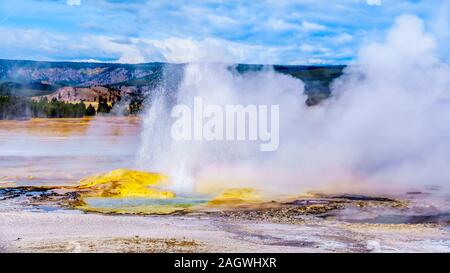 Wasser Herausspritzen des aktiven Jelly Geysir mit seinen gelben Schwefel mineral Berg im unteren Geyser Basin im Fountain Paint Pot Trail, Yellowstone Stockfoto