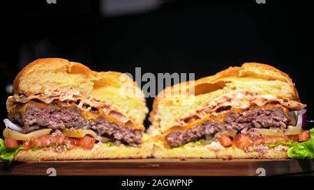 Schneiden Handwerk Burger ist Kochen auf schwarzem Hintergrund. Bestehen: Sauce, Salat, Tomaten, Roten Zwiebeln, Gurke, Käse, Speck, Brötchen und marmoriertes Fleisch Rindfleisch. Stockfoto