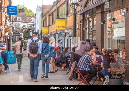 Eine Masse von Menschen außerhalb eines Cafe sitzen, mit anderen rund um Wandern in Perrin's Court, einer Seitenstraße in Hampstead, London, NW3, England, UK. Stockfoto