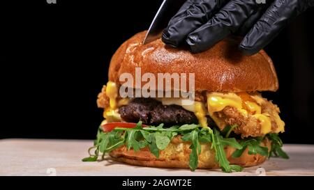 Schneiden Handwerk Burger ist Kochen auf schwarzem Hintergrund. Bestehen: sauce, Rucola, Tomaten, roten Zwiebeln Pommes, Gurken, Käse, Brötchen und Fleisch. Stockfoto