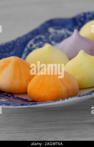 Baisers, verschiedene Farben, auf einem gemusterten blauen und weißen Platte. Graues Holz Hintergrund Stockfoto