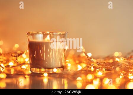 Brennende Kerze mit goldenen Girlande Lichter in Bokeh auf dunklem Hintergrund Stockfoto