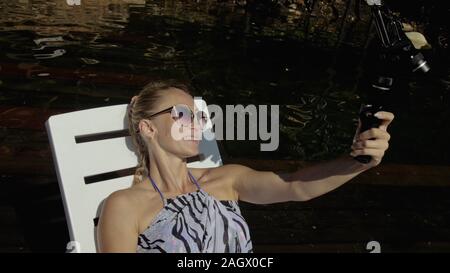 Frau schießen auf Handheld film Gimbal Stabilisierung für Smartphone. Mädchen liegen Liege auf Pier machen selfie. Blogger Broadcast Video vlogging. Stockfoto