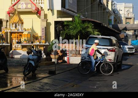 Ein Radfahrer im Gebiet des (Markt-)Pak Klong Talaat in Bangkok, Thailand, passiert ein traditionelles thailändisches Geistheiligtum oder Geisterhaus Stockfoto