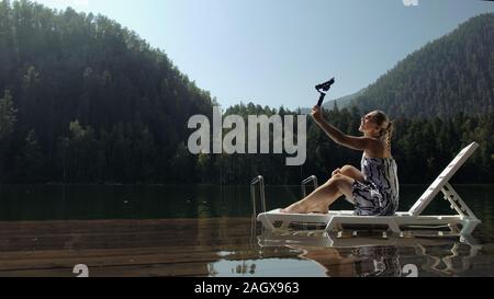 Frau schießen auf Handheld film Gimbal Stabilisierung für Smartphone. Mädchen liegen Liege auf Pier machen selfie. Blogger Broadcast Video vlogging. Stockfoto