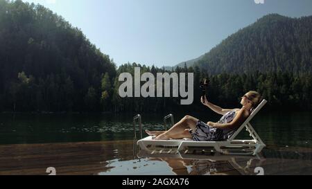 Frau schießen auf Handheld film Gimbal Stabilisierung für Smartphone. Mädchen liegen Liege auf Pier machen selfie. Blogger Broadcast Video vlogging. Stockfoto