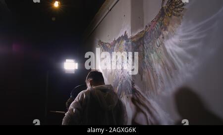 Künstler Designer zieht ein Adler an der Wand. Handwerker Dekorateur malt mit Acryl öl Farbe. Maler Maler gekleidet in Lack auftragen. Indoor. Stockfoto