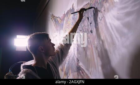 Künstler Designer zieht ein Adler an der Wand. Handwerker Dekorateur malt mit Acryl öl Farbe. Maler Maler gekleidet in Lack auftragen. Indoor. Stockfoto