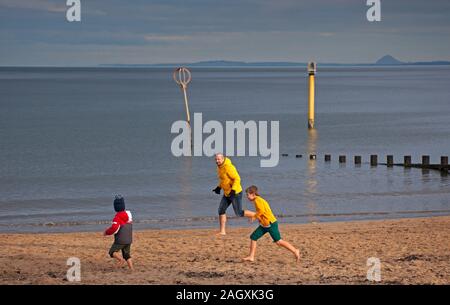 Portobello Beach, Edinburgh, Schottland, Großbritannien. 22. Dezember 2019. Kühle Temperaturen von 4 Grad mit geringem Sonnenschein an der Küste ermutigen die Menschen, jung und alt an der frischen Luft entlang der Sandstrand zu genießen. Bild Mann mit Jungen tig spielen beim Barfuss. Berwick Gesetz im Hintergrund. Credit: Bogen Weiß/Alamy Leben Nachrichten. Stockfoto