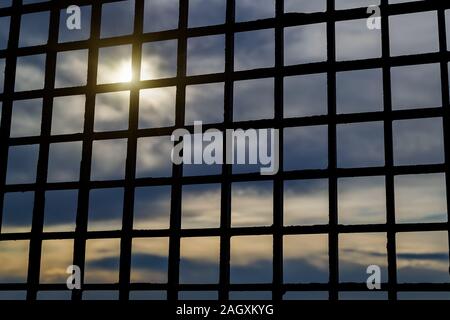 Durch die Bars in den Himmel schauen. Helles Sonnenlicht durch die dunklen Wolken brechen. Ins Gefängnis oder hinter der Bar sein. Das Konzept der Freiheit verlieren. Stockfoto