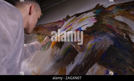 Künstler Designer zieht ein Adler an der Wand. Handwerker Dekorateur malt mit Acryl öl Farbe. Maler Maler gekleidet in Lack auftragen. Indoor. Stockfoto