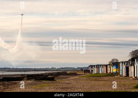 West Mersea, Mersea Island, Essex, Großbritannien. Ein Flugzeugpilot nutzte die Chance der Wetterpause, um über die Flussmündung des River Blackwater zu üben, um die Wanderer am Strand bei den bunten Strandhütten zu überraschen. Rauchspur Stockfoto