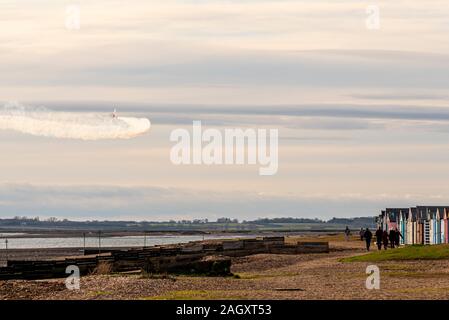 West Mersea, Mersea Island, Essex, Großbritannien. Ein Flugzeugpilot nutzte die Chance der Wetterpause, um über die Flussmündung des River Blackwater zu üben, um die Wanderer am Strand bei den bunten Strandhütten zu überraschen. Rauchspur Stockfoto