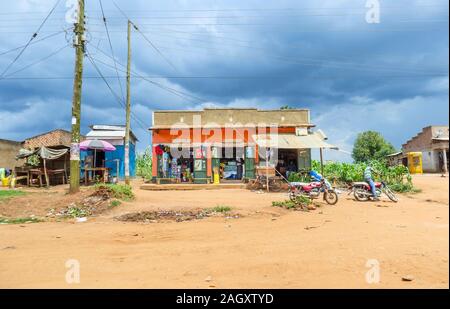 Typische Flachbau am Straßenrand Dorf Geschäfte mit einem General Store Shop und Gebäude mit der lokalen Bevölkerung in der westlichen Region von Uganda, an einem bewölkten Tag Stockfoto