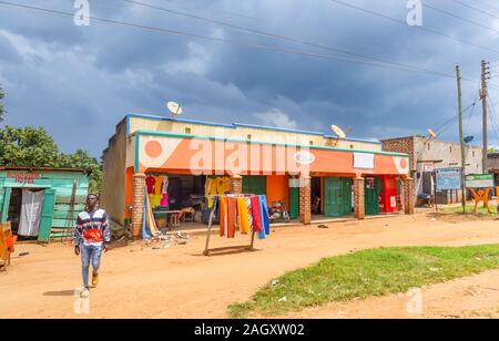 Typischen farbenfrohen Flachbau am Straßenrand Village Geschäften und Gebäuden für die lokale Bevölkerung in der westlichen Region von Uganda, an einem bewölkten Tag Stockfoto