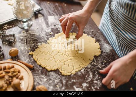 Cook Hausfrau die Weihnachtsplätzchen zu Hause auf eine bunte Küche. Weibliche Hände, Teig die Form der Weihnachtsbäume für den Urlaub Tabelle Stockfoto