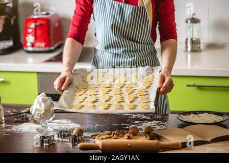 Cook Hausfrau die Weihnachtsplätzchen zu Hause auf eine bunte Küche. Eine Frau hält ein Backblech mit rohen Teig in der Form eines Weihnachtsbaumes bef Stockfoto