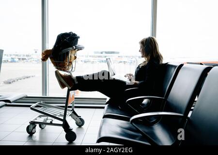 Ein kaukasischer blonde Frau wartet am Flughafen arbeiten mit Ihrem Laptop Stockfoto