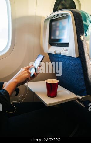 Detail der Hände einer Frau mit Handy im Flugzeug sitzen und Kaffee trinken Stockfoto