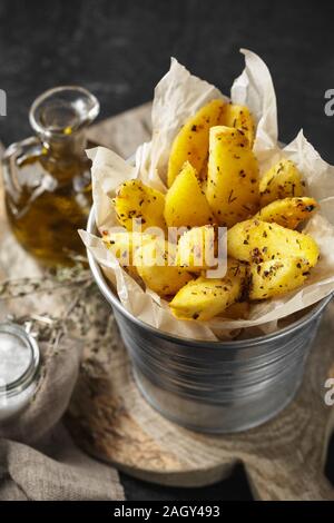 Gebackene Kartoffelecken in einem Metall Eimer mit Kräutern und Tomatensauce auf schwarzem Hintergrund - hausgemachte Bio Gemüse vegetarische Kartoffeln bereit sn zu essen Stockfoto