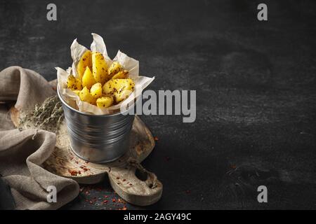 Gebackene Kartoffelecken in einem Metall Eimer mit Kräutern und Tomatensauce auf schwarzem Hintergrund - hausgemachte Bio Gemüse vegetarische Kartoffeln bereit sn zu essen Stockfoto