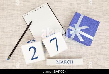 Kalender mit trendigen blau Text und Zahlen für März 27 und ein Geschenk in einer Box. Stockfoto