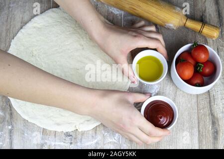 Eine Frau legt auf den Tisch mit Pizza und Cherry Tomaten Olivenöl Stockfoto