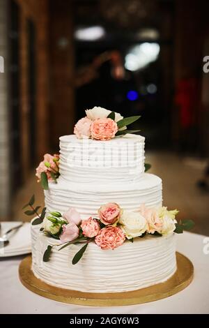 Weisse Hochzeitstorte mit rosa und weißen Blüten von Pfingstrosen und Rosen. Extra große dreistufige Hochzeitstorte mit weißen buttercream Frosting und Frische Stockfoto