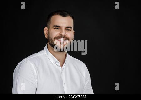 Close-up Portrait von lächelnden aussehenden bärtigen Mann an der Kamera schaut auf schwarzem Hintergrund Stockfoto