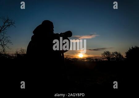 Die Silhouette des Fotografen mit Teleobjektiven Kamera gegen die Sonne, die herrlich an der Wintersonnenwende bei messwerteblock die South Point steigt in Co Wexford, Irland. Stockfoto
