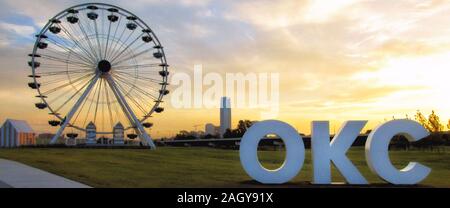 Wheeler Riesenrad und riesigen Schild stand out gegen einen Sonnenaufgang Himmel mit der Innenstadt von Oklahoma City im Hintergrund. Stockfoto