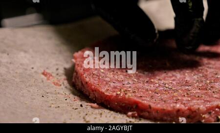 Kochen macht Fleisch Medaillons für Burger. Koch in schwarz Handschuhe macht Schnitzel essen. Die koteletts sind in Stahl Ring in eine noch Medaillon eingeebnet. Stockfoto
