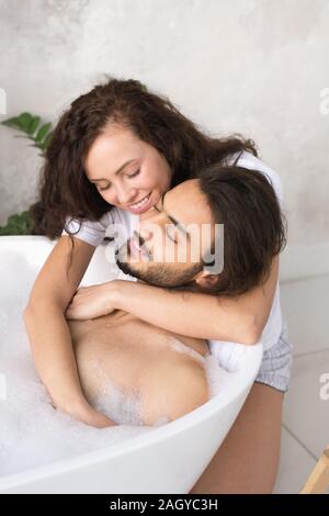 Glückliche junge liebevolle Frau, die ihren Mann entspannt genießen, Badewanne Stockfoto