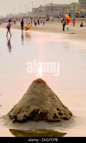 PURI, Orissa/Indien - 5. MÄRZ 2018: eine handmad Vulkan geformten Haufen Sand sitzt auf dem nassen Sand mit der Sonne hinter Einstellung. Stockfoto