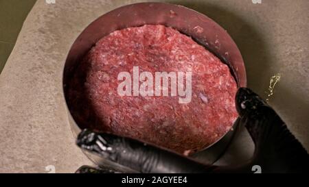 Kochen macht Fleisch Medaillons für Burger. Koch in schwarz Handschuhe macht Schnitzel essen. Die koteletts sind in Stahl Ring in eine noch Medaillon eingeebnet. Stockfoto