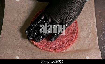 Kochen macht Fleisch Medaillons für Burger. Koch in schwarz Handschuhe macht Schnitzel essen. Die koteletts sind in Stahl Ring in eine noch Medaillon eingeebnet. Stockfoto