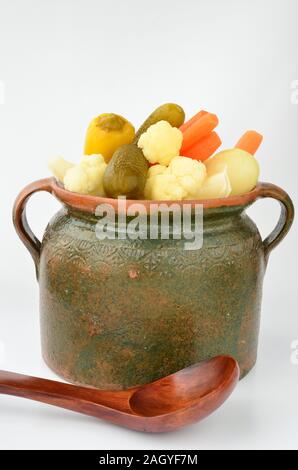 Eingelegtes Gemüse in einen Tontopf mit einem hölzernen Löffel auf weißem Hintergrund Stockfoto