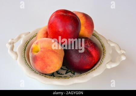 Haufen frische Pfirsiche in rustikalen Keramik Obstschale auf weißem Hintergrund Stockfoto