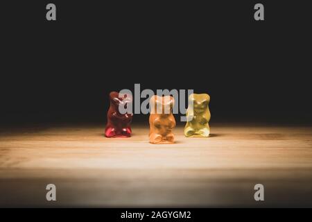 Ein Porträt von drei unterschiedlichen farbigen Gummibärchen, die Candy steht auf einem Holzbrett mit Beleuchtung, das aussieht, wie sie auf der Bühne sind. Stockfoto