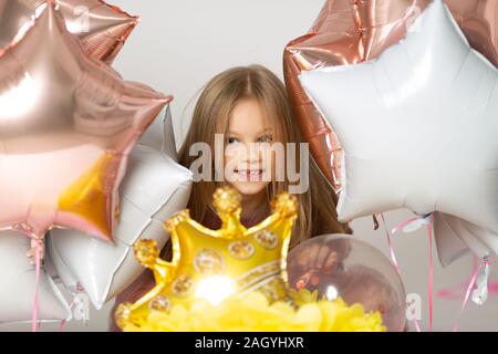 Blauäugigen blonden lacht und zeigt erste Zahn. Nettes Mädchen auf weißem Hintergrund und Ballons Stockfoto