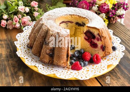 Kugelhopf mit Beeren auf einem rustikalen Holztisch. Stockfoto