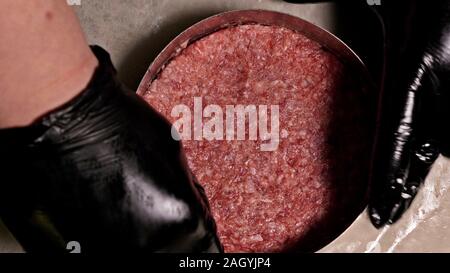 Kochen macht Fleisch Medaillons für Burger. Koch in schwarz Handschuhe macht Schnitzel essen. Die koteletts sind in Stahl Ring in eine noch Medaillon eingeebnet. Stockfoto