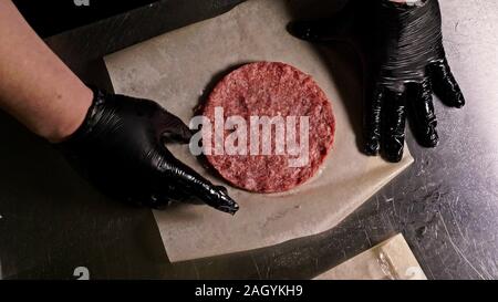 Kochen macht Fleisch Medaillons für Burger. Koch in schwarz Handschuhe macht Schnitzel essen. Die koteletts sind in Stahl Ring in eine noch Medaillon eingeebnet. Stockfoto