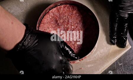 Kochen macht Fleisch Medaillons für Burger. Koch in schwarz Handschuhe macht Schnitzel essen. Die koteletts sind in Stahl Ring in eine noch Medaillon eingeebnet. Stockfoto