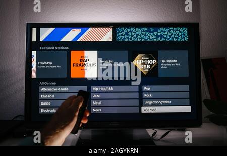 Paris, Frankreich, ca.2019: Mann mit Remote Apple TV Menü auf Panasonic Plasma tv Wohnzimmer mit Fatured Stationen in allen Genres große playlist Surf von Apple Musik Stockfoto