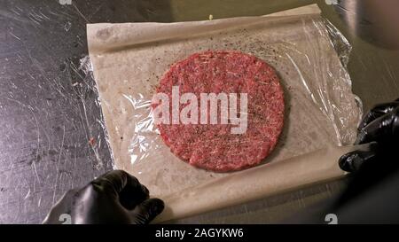 Kochen macht Fleisch Medaillons für Burger. Koch in schwarz Handschuhe macht Schnitzel essen. Die koteletts sind in Stahl Ring in eine noch Medaillon eingeebnet. Stockfoto
